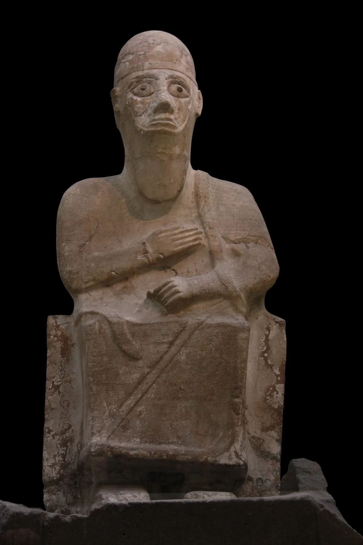 Seated white stone statue of a king covered in cuneiform text