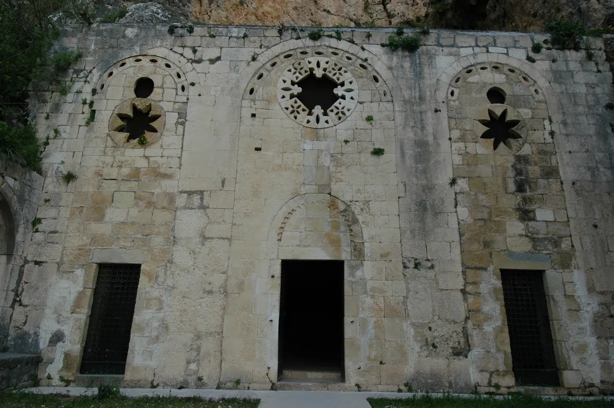 A stone façade with three arched openings set into a rocky mountainside