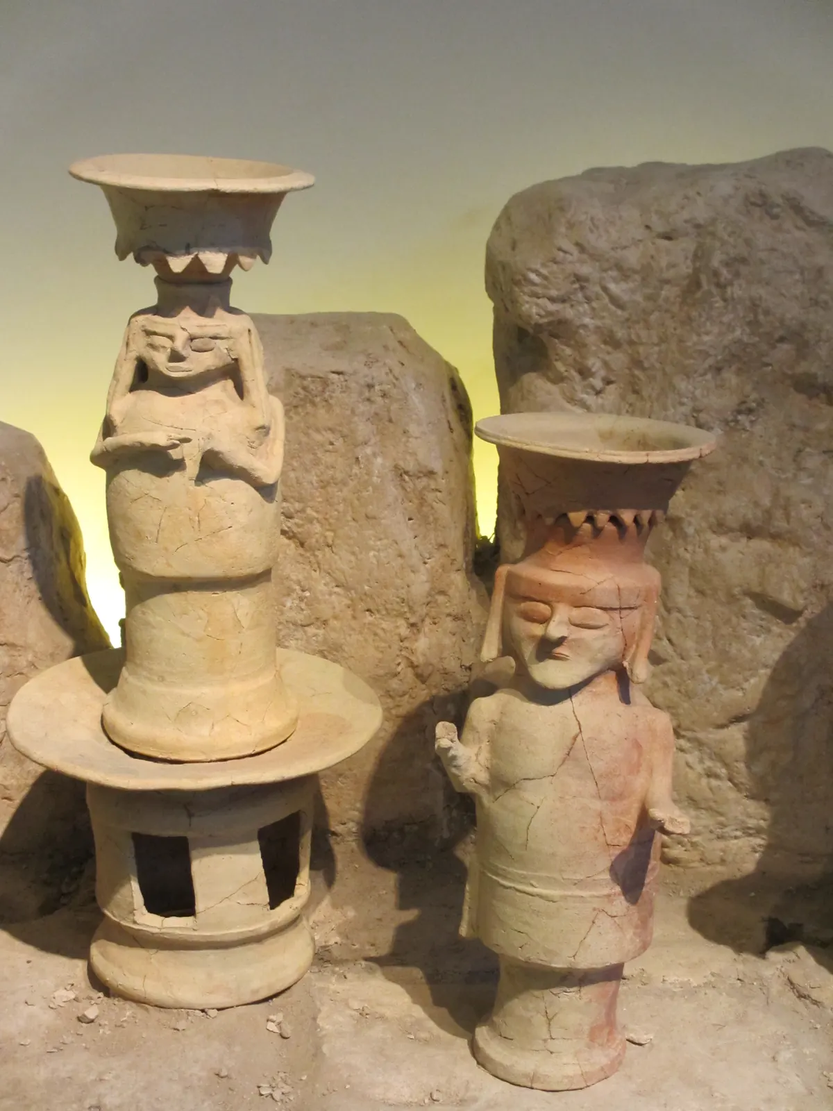 Tall painted clay cult stands with human features in a museum case