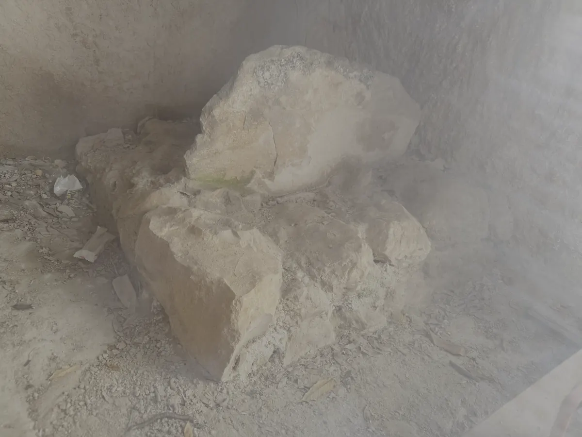 A large upright limestone block set against the bedrock wall of a rock-cut room