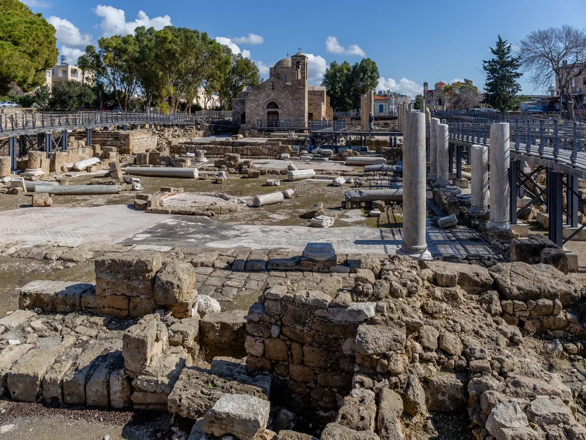 A stubby marble column standing amid basilica ruins near a small stone church