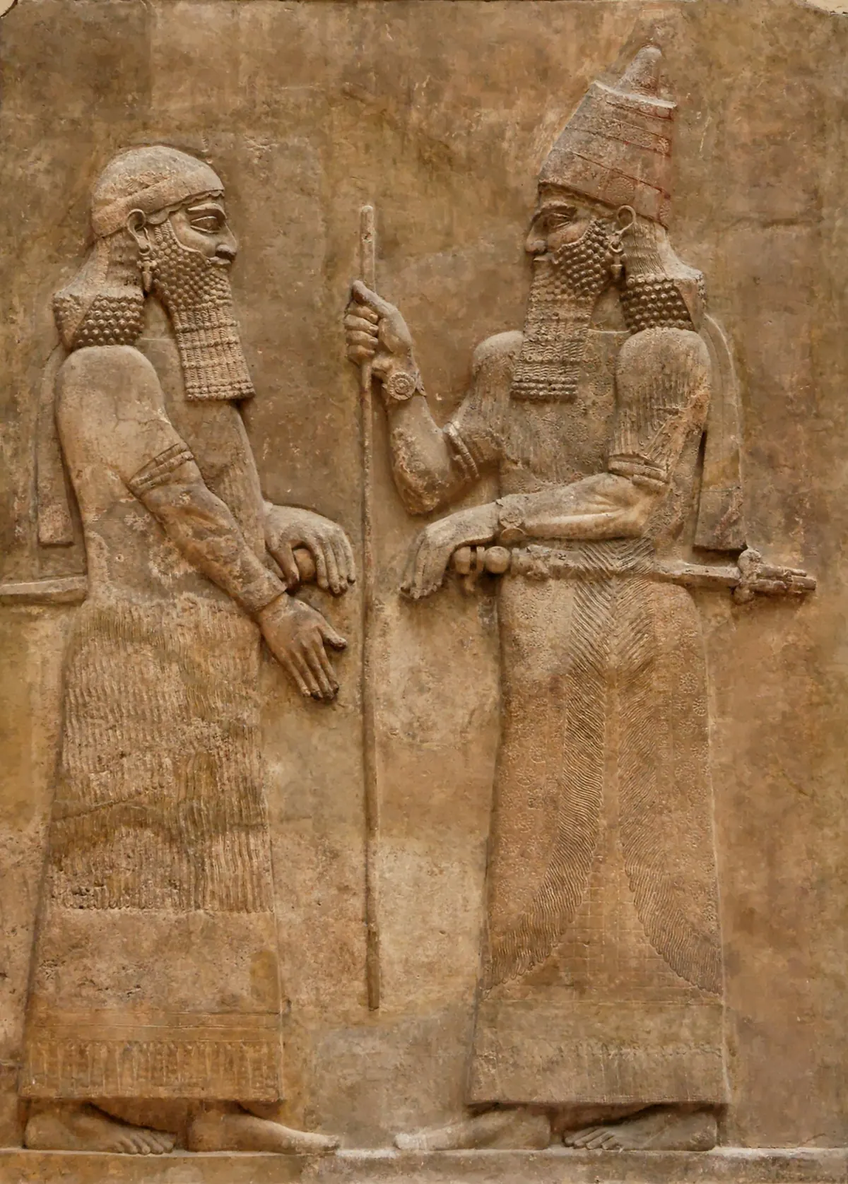 Assyrian relief of a bearded king holding a staff, facing an official