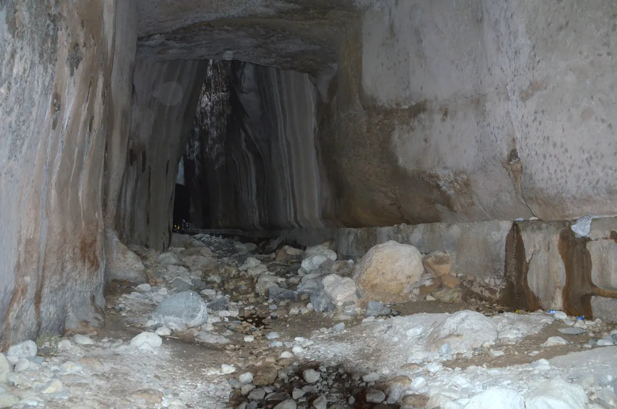 A deep man-made gorge cut through rock, with a dark tunnel mouth ahead