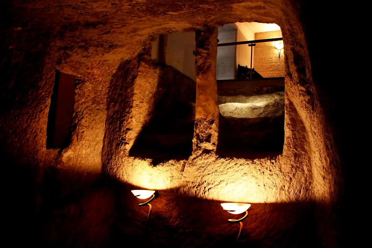 Deep rock-cut chamber lit from above, with carved crosses on the walls