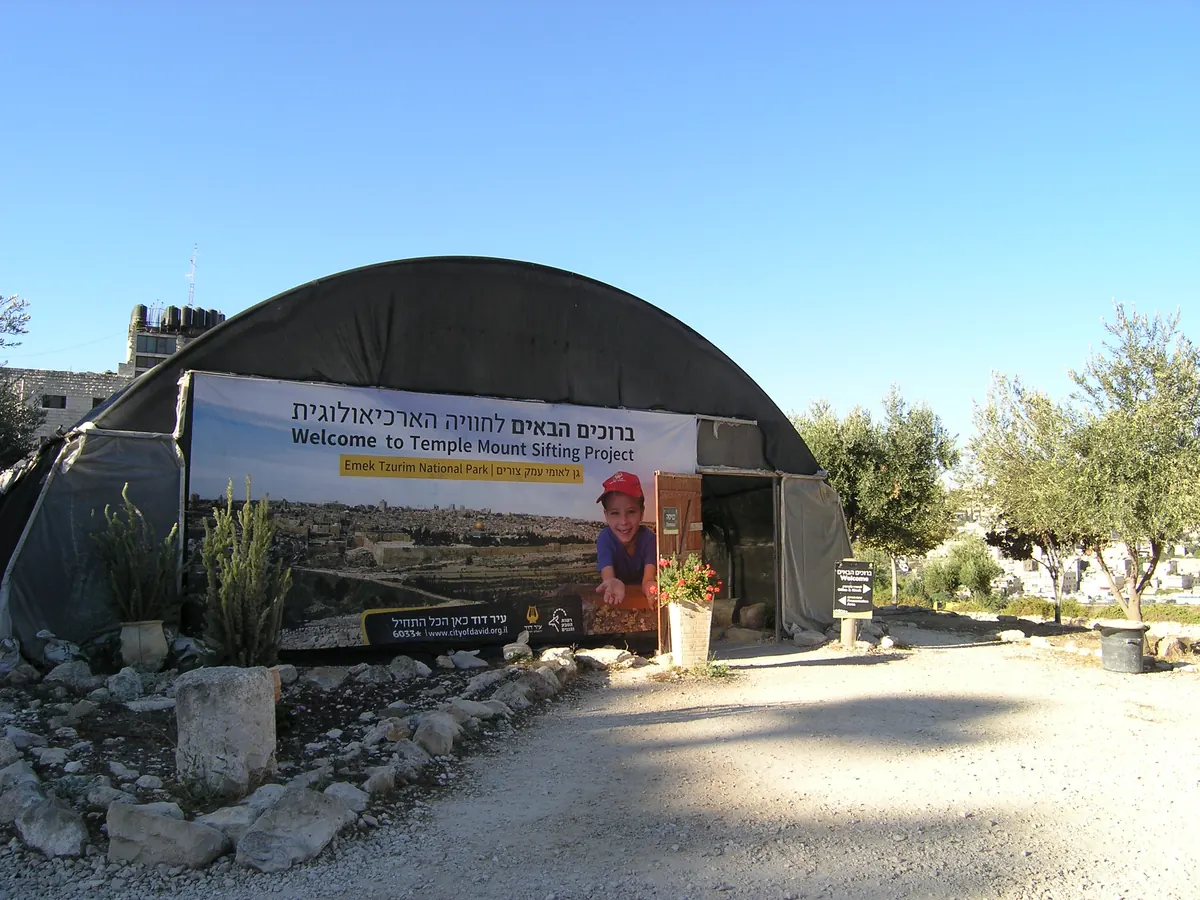 People sifting soil through screens under a shade tent